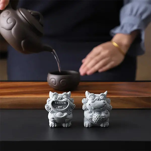 Duo de Chien Fu Statuettes Lion Gardien Chinois en Grès sur une table en bois avec une théière en arrière plan kaosix